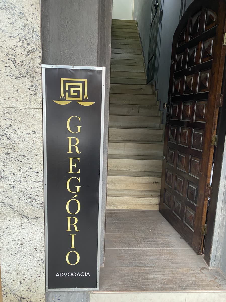 Entrada do escritório: placa preta e dourada com a marca Gregório Advocacia, ao lado da porta de madeira.